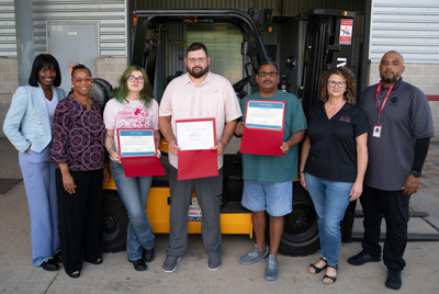 Three students hold certificates, while several staff members pose for a photo with them.